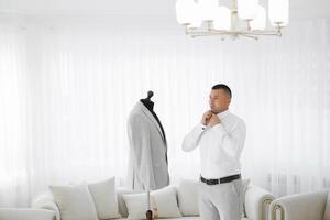 A man is getting ready to tie his tie in front of a mannequin dressed in a strip photo