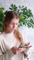 mulher usando Smartphone às casa com grande quantidade do plantas, pensativamente digitando uma mensagem e olhando fotos video