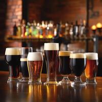 Various types of beer in different shaped glasses placed on a bar counter, showcasing a range of beers from light golden to deep amber and dark brown photo