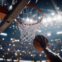 action shot of a basketball being dunked into the hoop by a player's hand, with the ball just about to pass through the net. photo