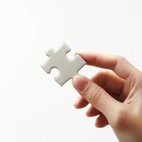hand holding a single puzzle piece against a clean, pure white isolated background. The hand is well-defined with natural skin tones and soft lighting, creating subtle shadows for a realistic effect photo