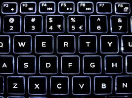 A close-up of a backlit keyboard with illuminated keys in a QWERTY layout. White letters on black keys contrast sharply, showcasing a sleek, modern design with a smooth, polished finish. photo
