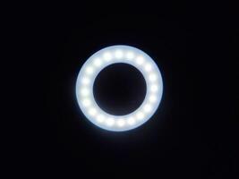 A circular LED ring light glows softly against a dark background, with evenly spaced bulbs ideal for photography, videography, or content creation. Perfect for themes of lighting, tech, or creativity. photo