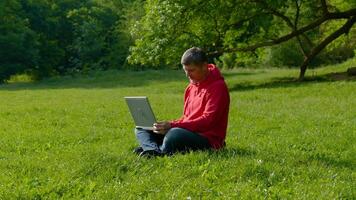 Man working on laptop in summer forest At The Sunny Day. Busy freelance worker is tired and wants to rest. Freelancer Remote Work Concept. 4K video