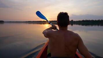 A man kayaks on a calm river towards the sunset. He skillfully rowing oar. Beautiful nature of the evening river. Super Slow Motion video