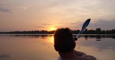 A man kayaks on a calm river towards the sunset. He skillfully rowing oar. Beautiful nature of the evening river. Slow Motion Ultra 4K 50 fps video