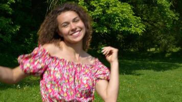 Woman dancing in dress on the lawn in summer park. Happy smiling girl enjoy life spinning around. Slow motion video