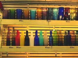 Colorful of glass, bottle and vase on wooden shelf for sale at dishware store or shop in yellow tone. Design object photo