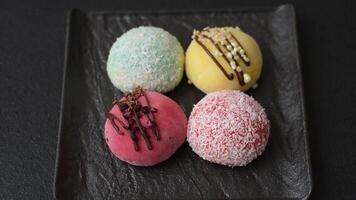 Delicious colorful asian mochi sweets with rice dough shell and fruit filling on dark concrete background video