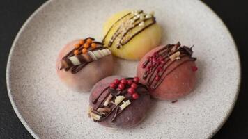 Delicious colorful asian mochi sweets with rice dough shell and fruit filling on dark concrete background video