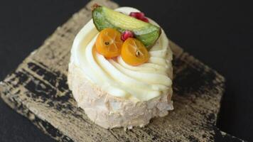 Piece of sweet meringue with citrus, kiwi and pomegranate seeds on a dark concrete background video