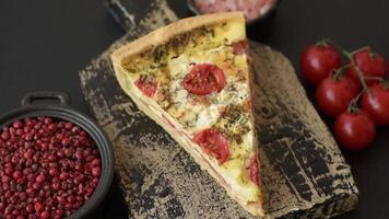 Delicious crispy quiche cut into slices with cheese, broccoli, tomatoes, salt, spices and herbs on a dark concrete background video