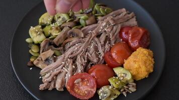 Boiled beef with vegetables, grains, seeds and spices in a ceramic plate on a dark concrete background video