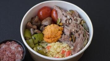 Boiled beef with vegetables, grains, seeds and spices in a ceramic plate on a dark concrete background video