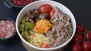 Boiled beef with vegetables, grains, seeds and spices in a ceramic plate on a dark concrete background video