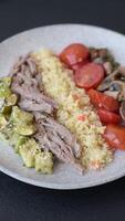 Boiled beef with vegetables, grains, seeds and spices in a ceramic plate on a dark concrete background video