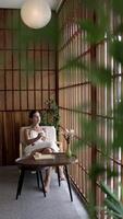 Young, caucasian woman enjoying a cup of coffee, tea lounge chilling near window in modern cozy apartment. Relaxed serene brunette girl feel fatigue lounge on comfortable sofa at home. video