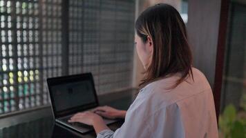 Woman sits at a desk with a laptop, working on a project. The image is focused on the woman's hands and the laptop, and the background is blurred. video