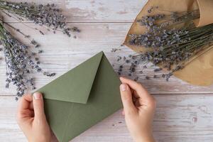 Flat lay composition of female hands holding green envelope with dry lavender flowers. Copy space template mock up. Top view. Concept of Wedding invitation postcard. Business advertisement brand blank photo