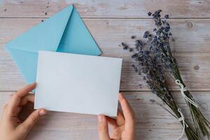Flat lay composition of white paper greeting card on envelope with dry lavender flowers. Copy space template mock up. Top view. Concept of Wedding invitation postcard. Business advertisement brand blank photo