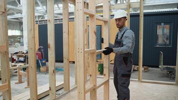 Carpenter in uniform installing wooden frame in prefabricated modular house in construction site video