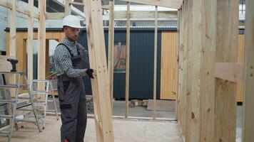 Carpenter engineer in uniform installing wooden frame in prefabricated modular house in construction site video