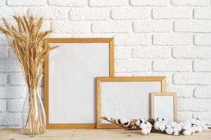 Vase with ears of wheat and photo frames against brick wall