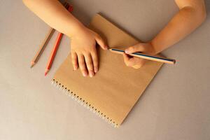Kid's hands writing in open notebook, top view, copy space photo