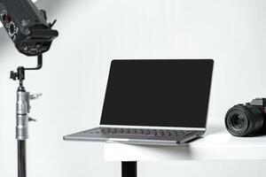 Laptop with black screen and photography equipment in photostudio photo