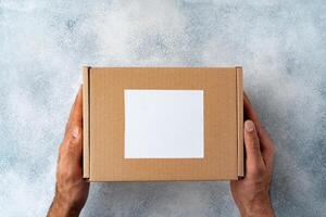 Parcel cardboard box in a man hands on a gray table background photo