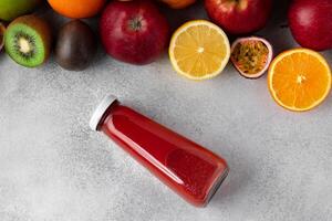 Various fruits and freshly squeezed fruits juice in bottle on gray background photo