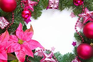 Festive Christmas arrangement featuring pink poinsettia, fir branches, pink and fuchsia ornaments, glittering stars and beads with empty white space in the center for text for holiday themed projects photo