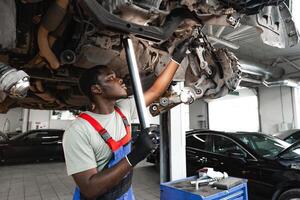 Young African mechanic in uniform working under the car in car service center photo