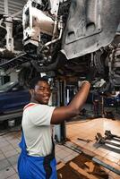 Young African mechanic in uniform working under the car in car service center photo