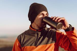Young man traveler drinking from his thermocup while halt on a hike photo