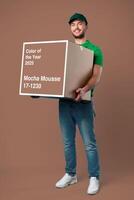 Person holding a large box labeled Mocha Mousse Color of the Year 2025 in a studio with a neutral background photo