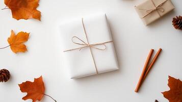 White gift box wrapped with twine surrounded by autumn leaves and decorative elements on a light background photo