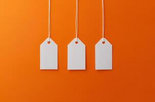 Three Blank White Price Tags Hanging on an Orange Background photo
