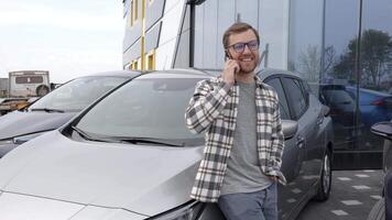 Handsome young man talking on the mobile phone and smiling while leaning at his car video