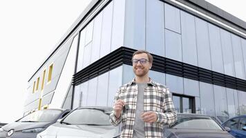 Emotional guy holding key in hand and smiling at camera. Man showing key from his new electric car. Young man buying auto at dealership salon video