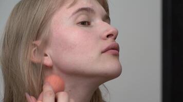 Young woman is using makeup brush to apply cream foundation to her face for stage makeup and looking in mirror. Cream foundations are ideal for dry skin as they provide hydration and luminous finish video