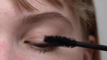 Young woman is using tip of mascara brush to apply the product and prevent clumping. Mascara is intended to enhance and add depth to lashes. Shot is an extreme close-up view process, handheld video