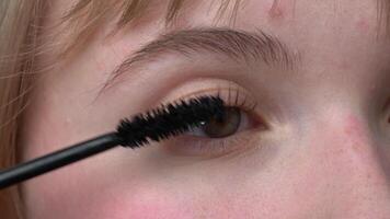 Woman with brown eyes shown in an extreme close-up applying mascara to her lashes. She uses only tip of brush to prevent clumping. Mascara is designed to intensify, add depth to look. Extreme closeup video