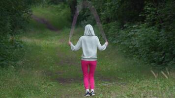 Rear view of unrecognizable woman training with skipping rope, doing warm up exercises. Full length of athlete in sports clothes during summer training with jumping rope, physical training in open air video