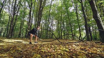 Man with battle rope in park. Athletic young man with battle rope doing exercise video