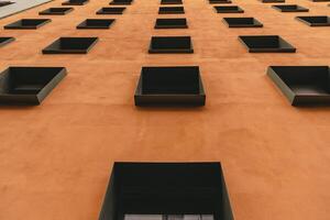 Contemporary building with terracotta color wall and rows of windows in metal frames. Modern architecture of Berlin Germany. Low angle view to facade exterior. Urban geometric pattern photo