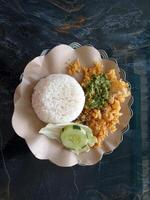 Top view of a plate of rice and ayam geprek, literally translated smashed chicken, with a slice of cucumber, cabbage and green chili sauce. photo