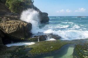 Big waves crashed against rocks and cliffs. Beautiful bay with natural pond in Tulungagung, East Java, Indonesia. photo