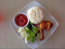 Flat lay view of plated fried chicken with rice, vegetables and sambal or chili sauce. photo