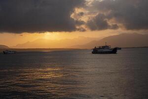 A passenger ship sailing in the Bali Strait with the cloudy sunrise and the silhouette of mountain formations in the background. photo